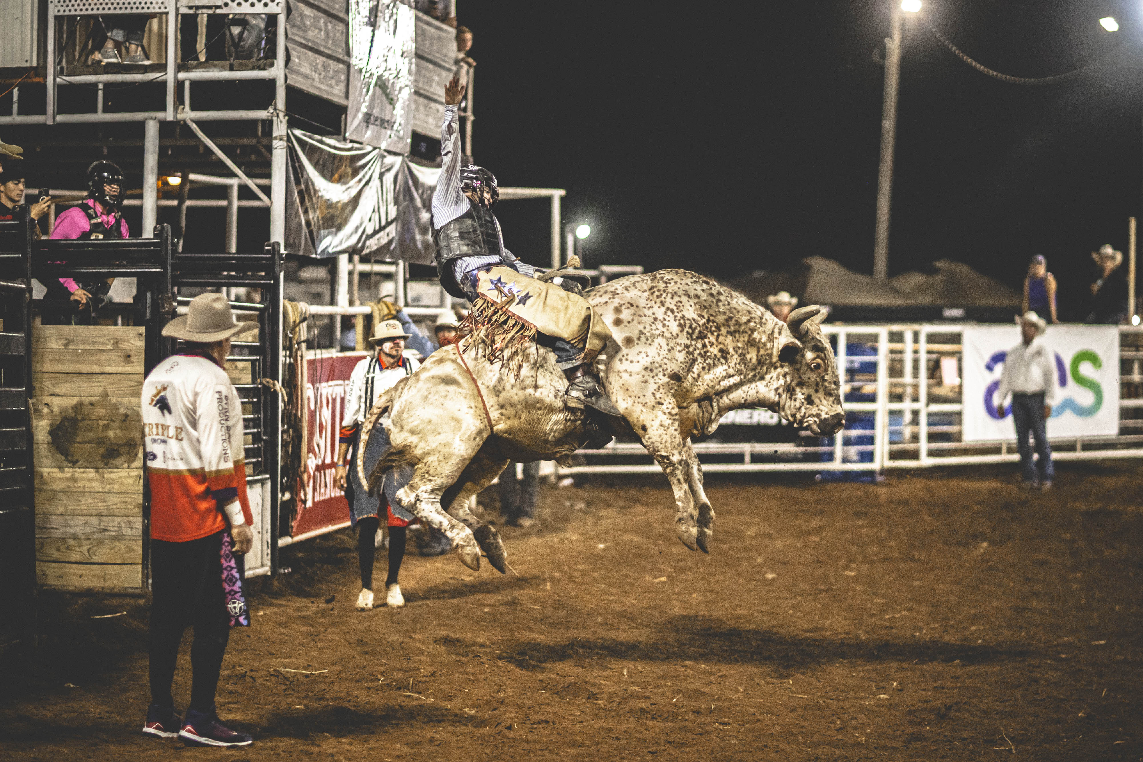 A bull rider explodes out of the chute during the 2025 Fisher County Fair & Rodeo, holding on as the bull catches air under the arena lights. Photo by Mark Martinez