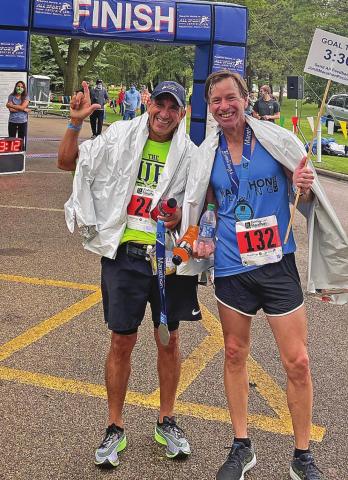 Julio Carrillo flashes Texas Tech's "Guns up" as he stands alongside a pacer at the finish line of the Brookings SD, where Carrillo earned his BQ of 3:28:43. A pacer is a runner that qualifies in a higher bracket, but volunteers to run in a slower bracket to assist and encourage other runners along the route.