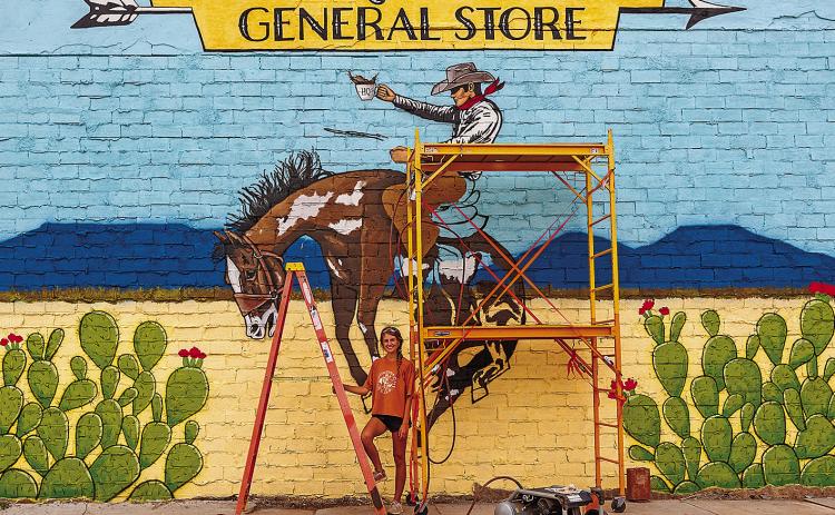 Artist Lexi Haag stands in front of her largest work yet, which graces the the main-street-facing wall of the Headquarters General Store's new location.