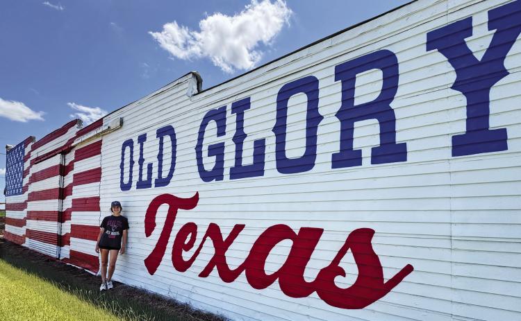 Lexi Antonick stands in front of the newly refreshed Old Glory mural she restored.