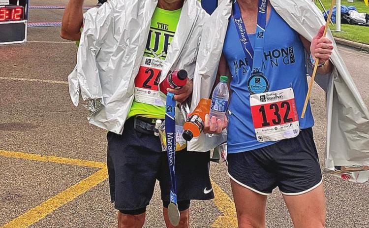 Julio Carrillo flashes Texas Tech's "Guns up" as he stands alongside a pacer at the finish line of the Brookings SD, where Carrillo earned his BQ of 3:28:43. A pacer is a runner that qualifies in a higher bracket, but volunteers to run in a slower bracket to assist and encourage other runners along the route.